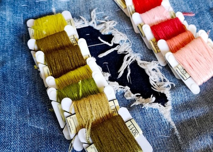 Denim mending with running stitch, colored embroidery floss on bobbins