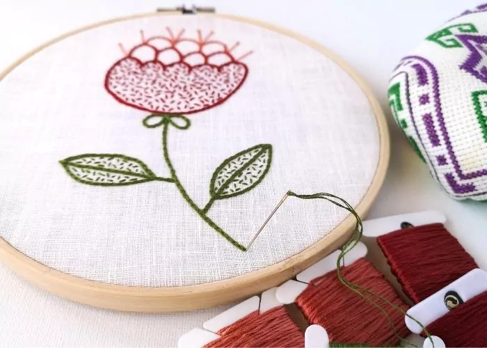 Red abstract flower embroidery in a hoop, needle with green thread and bobbins of red floss