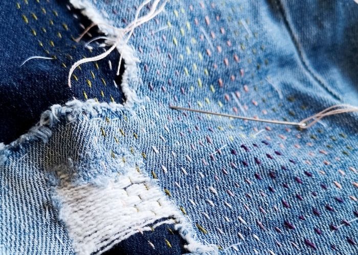 Mending holes in jeans by hand with running stitch