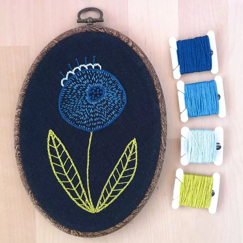 Blue modern flower embroidery on dark fabric in an oval hoop