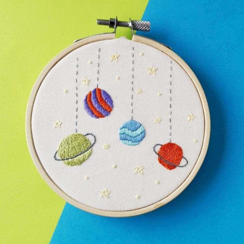 Colorful planets embroidered on white cotton canvas. Framed in a hoop. On bright blue and green background