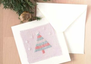 Postcard with Christmas tree embroidery on pink linen, white envelope and pine cone