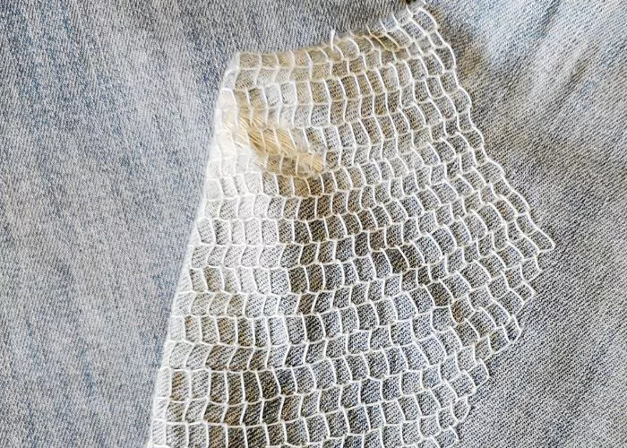 A net like stitch in white thread on denim fabric, a type of mending technique