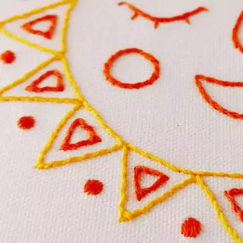 Detail of hand embroidered sun image - bright yellow threads on white linen