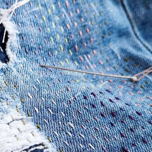 Mending jeans with running stitches. Blue denim fabric and a needle.