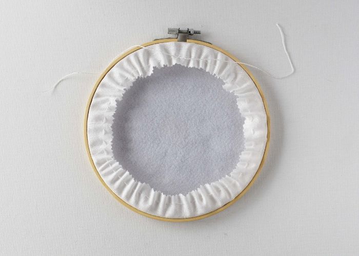 Back of the hoop with fabric gathered with running stitches