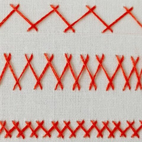 Herringbone stitch embroidery with red floss on white fabric