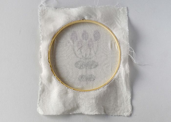 The back of the hoop with white backing fabric trimmed close to the edge of the hoop