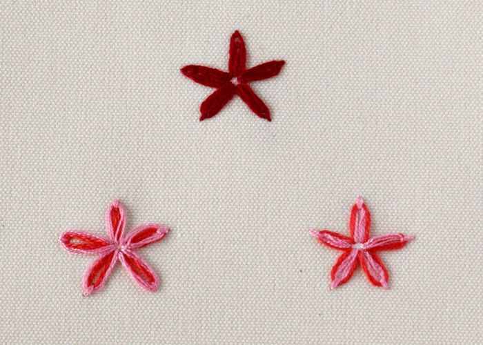 Three flowers embroidered with Lazy Daisy embroidery stitch in red and pink colors