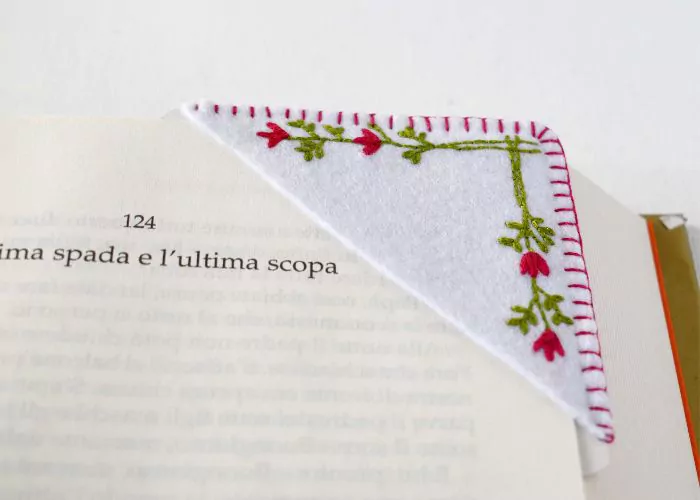 Hand embroidered corner bookmark with minimalist flowers placed on a book