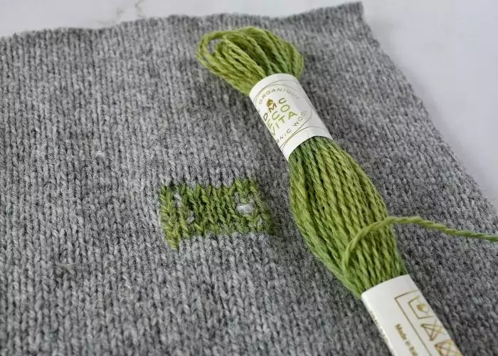 Swiss darning on knitwear with green wool threads image