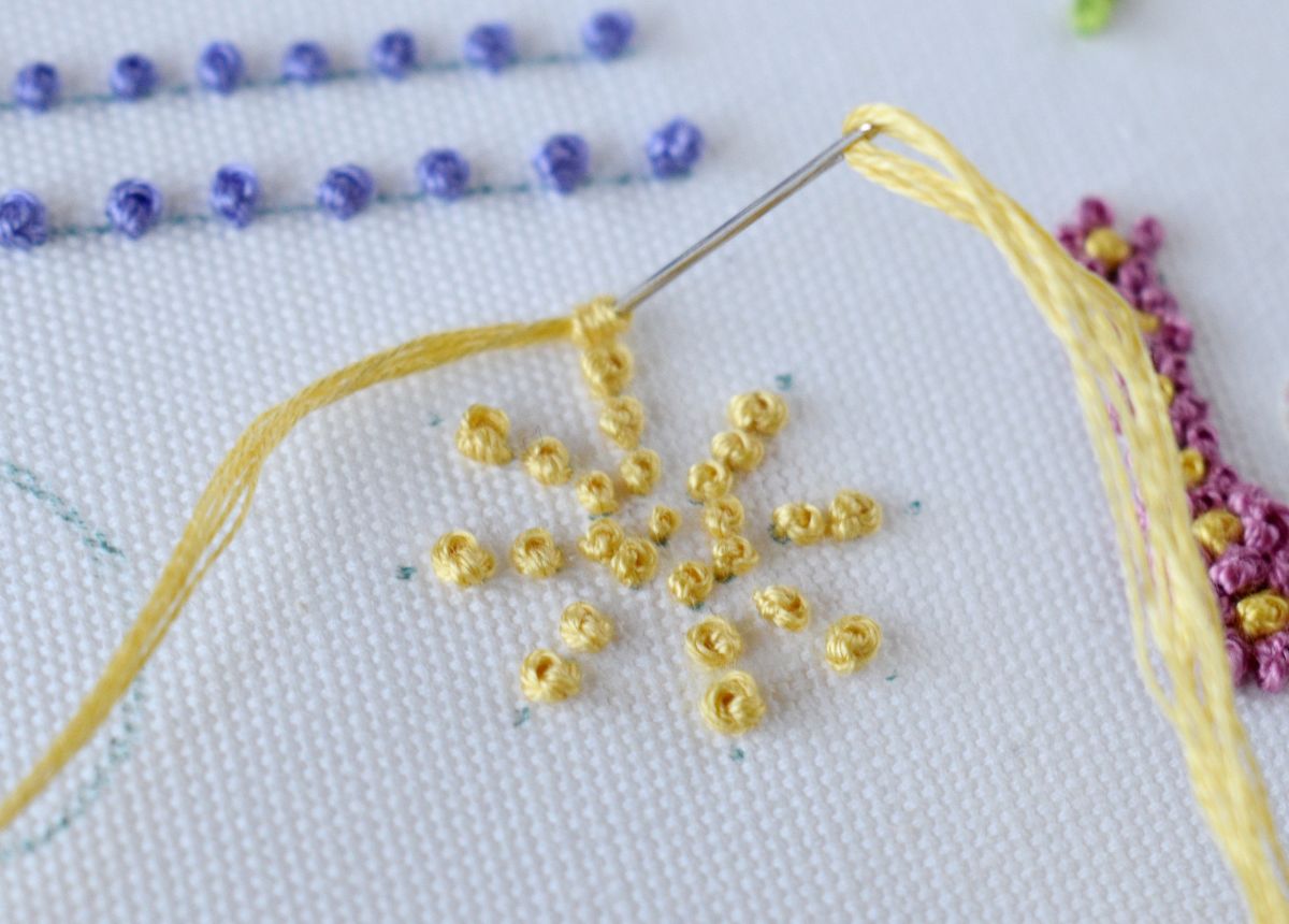 Yellow snowflake shape embroidery with french knots on white fabric
