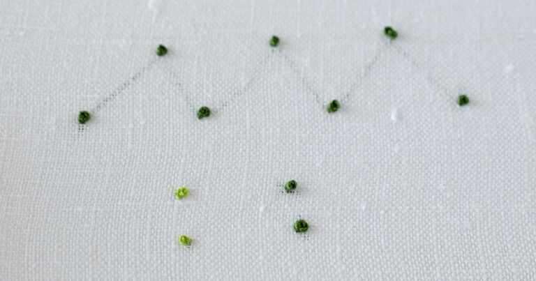 image of isolated french knot stitches with trailing between the stitches and without. Green floss on white fabric