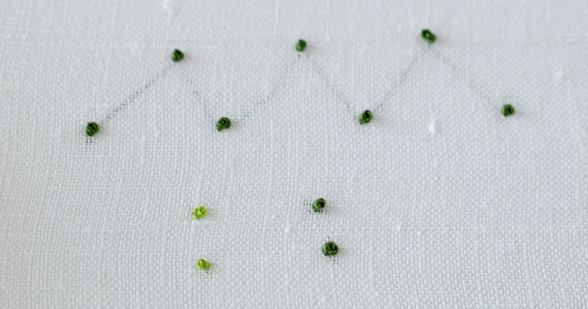 image of isolated french knot stitches with trailing between the stitches and without. Green floss on white fabric