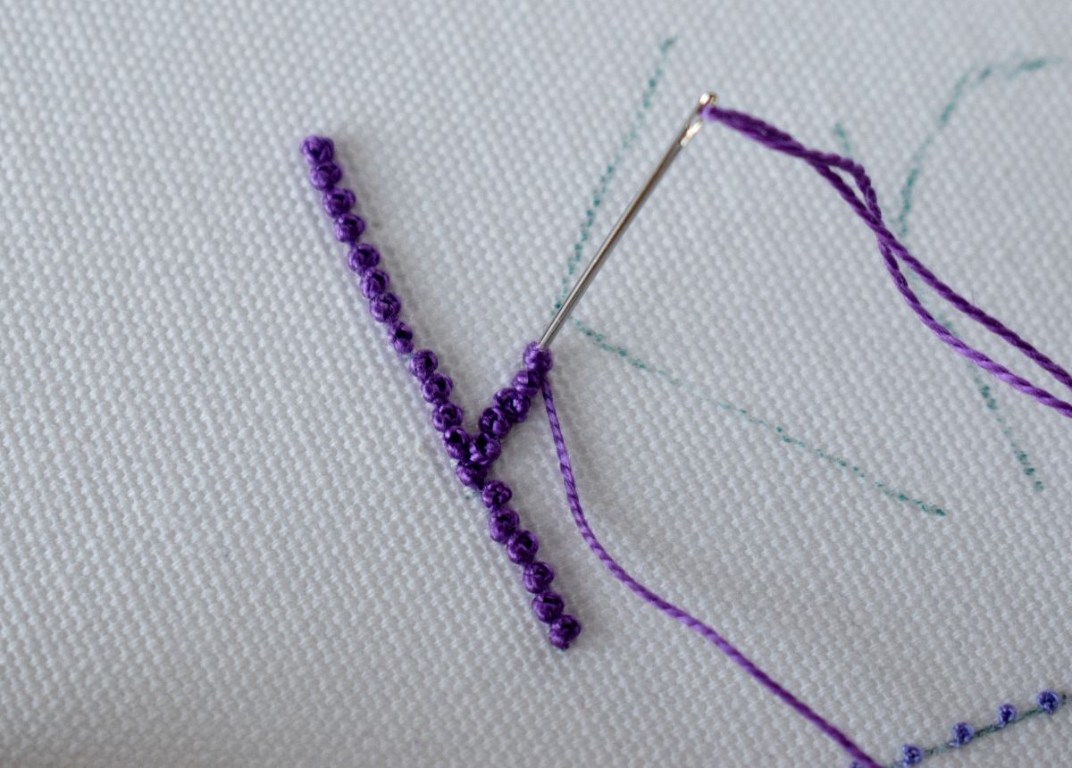 Letter K embroidery with french knot technique using purple pearl cotton on white fabric