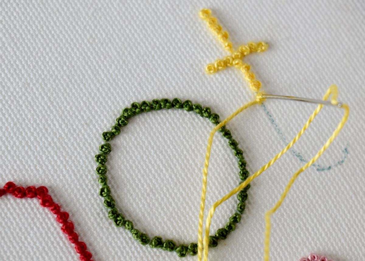 Letter t embroidery progress with yellow pearl cotton and french knot technique on white fabric