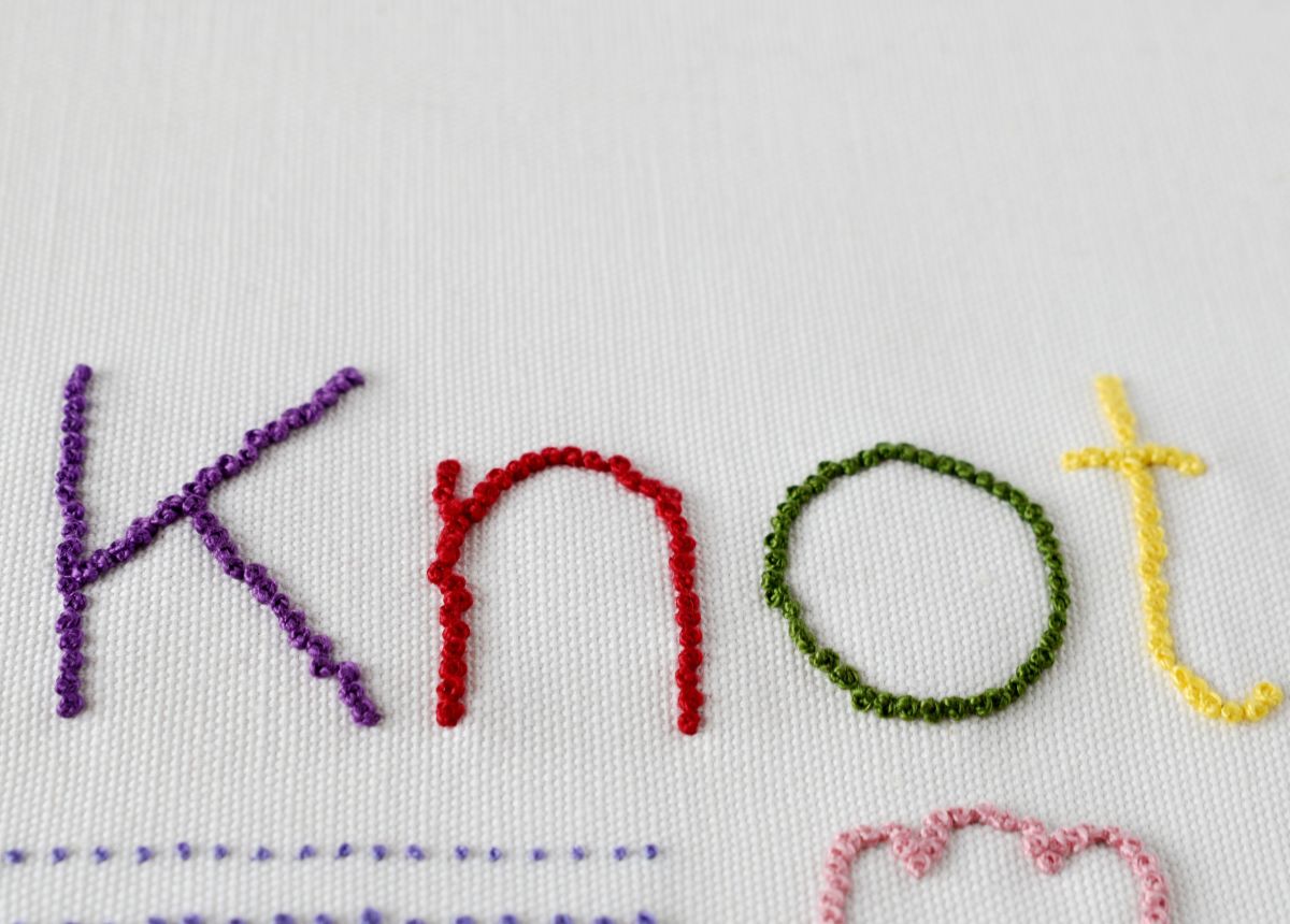 word knot hand embroidered with French Knots in different colors on white fabric