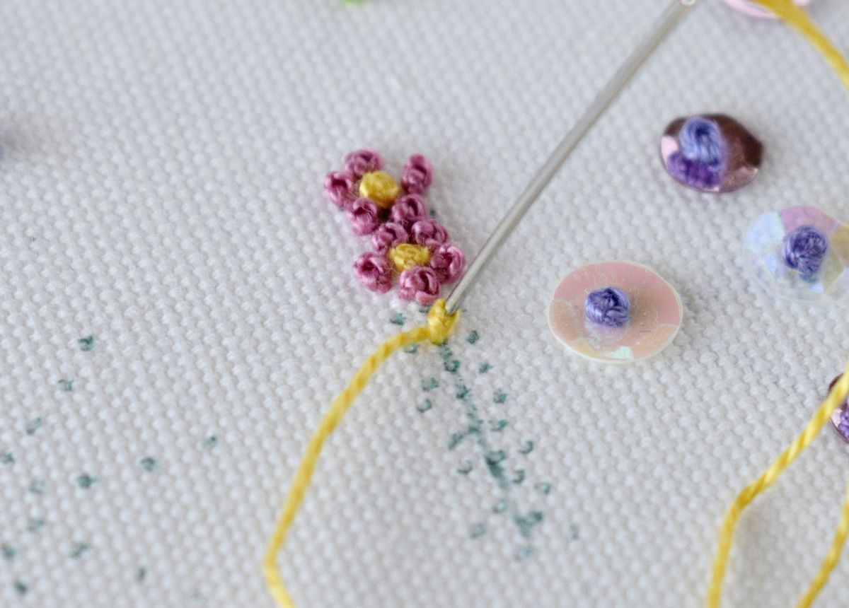 Micro flowers hand embroidery with French Knot technique in pink and yellow pearl cotton on white fabric