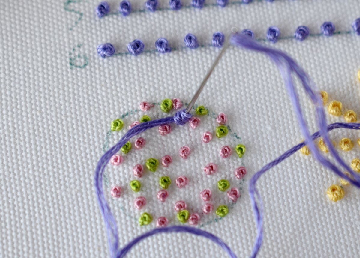 French knots of various sizes and colors filling the circle shape on white fabric